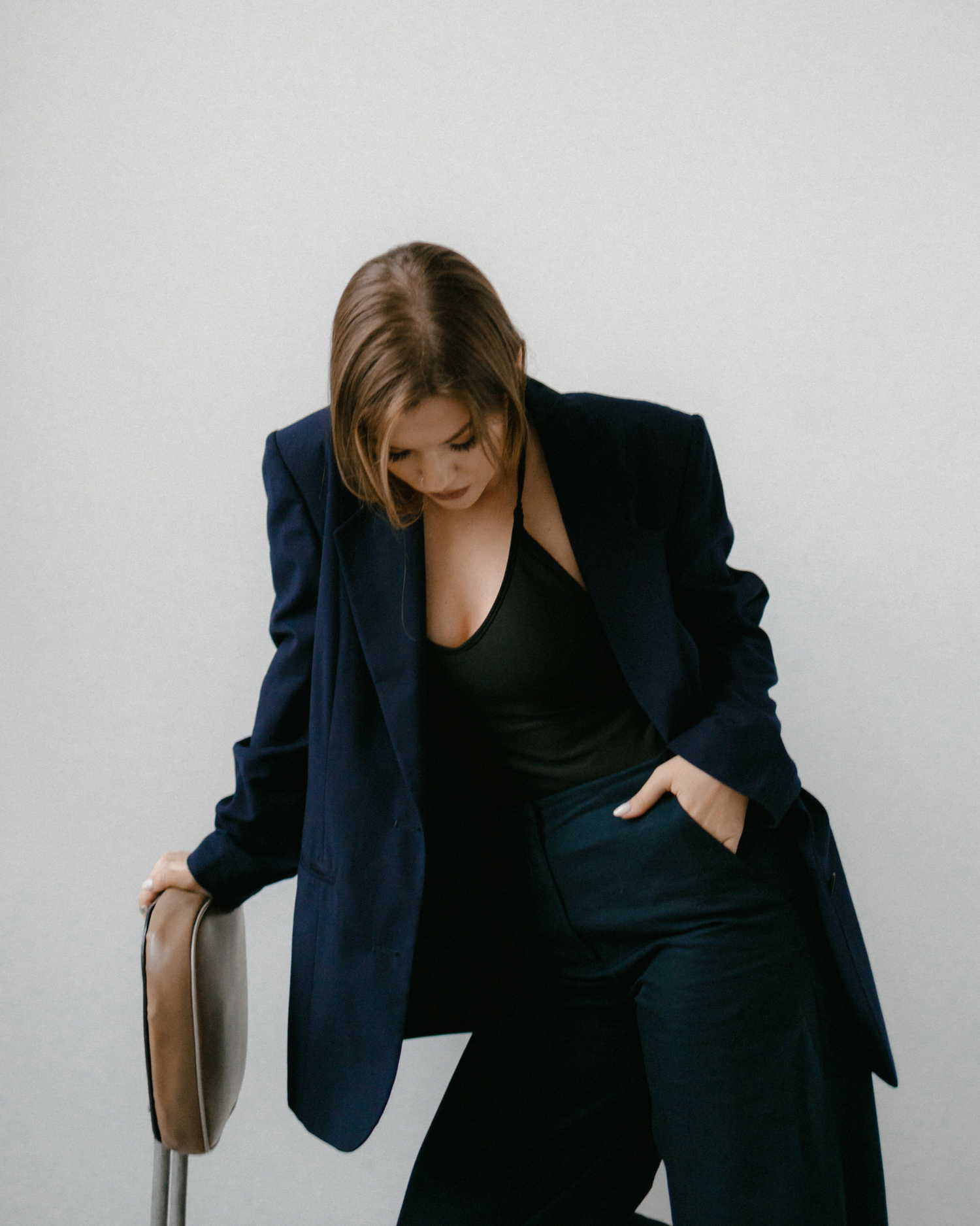 Model wearing a blue suit looking down while kneeling on a brown chair 