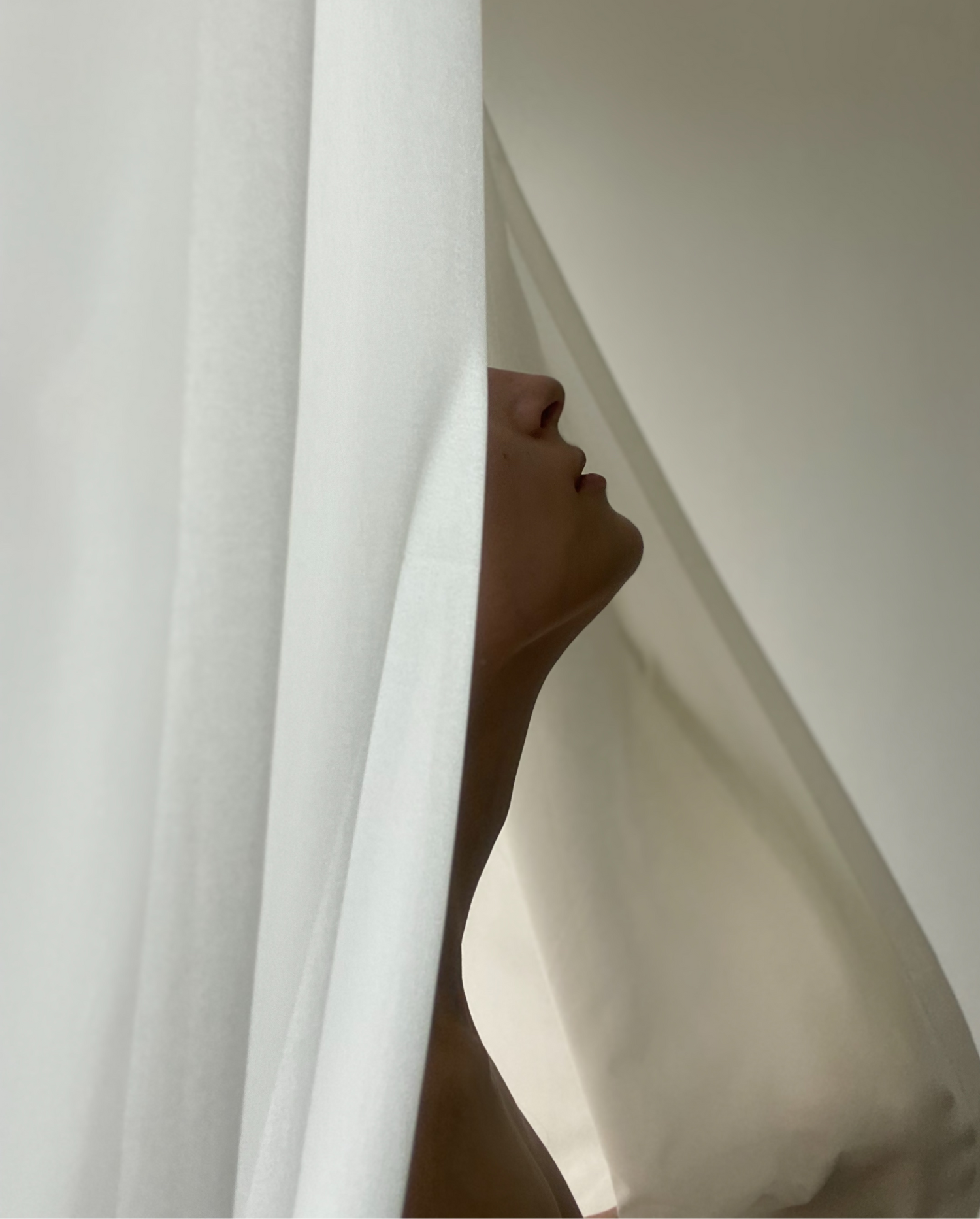 Model standing in a white curtain with chin and nose showing 