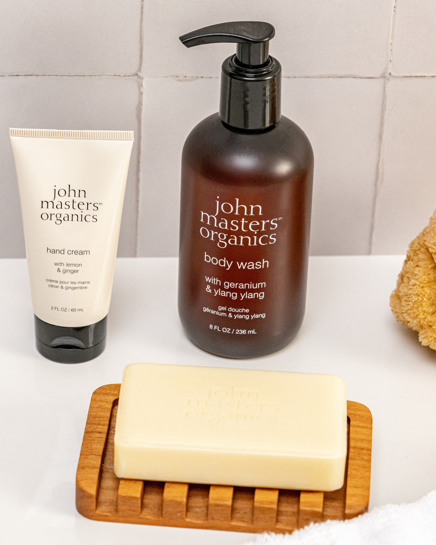 John Masters Organics Hand Cream, Body Wash, and Bar Soap with sponge on bathroom counter